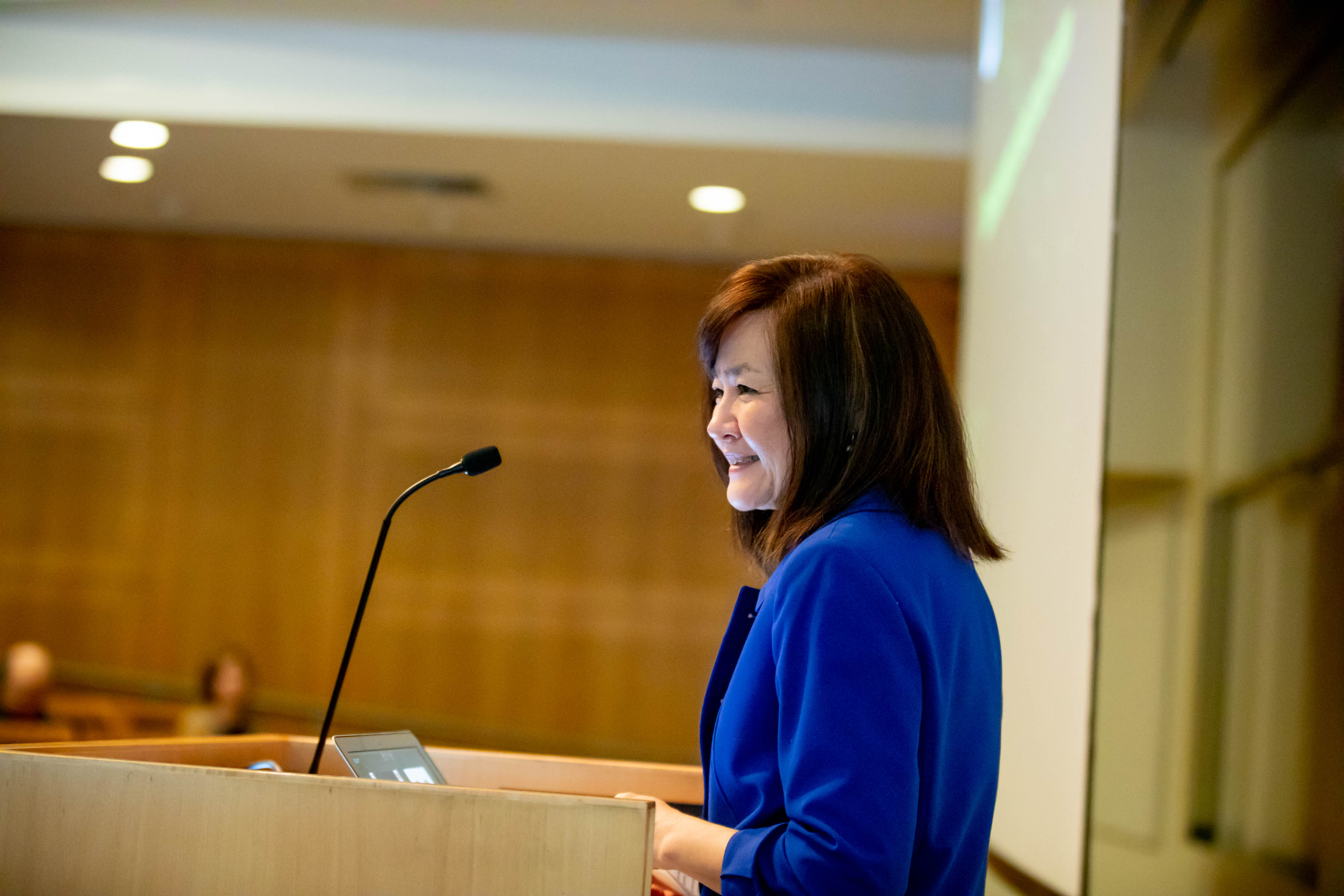 Li-Huei Tsai smiles in a profile view as she stands at a lectern