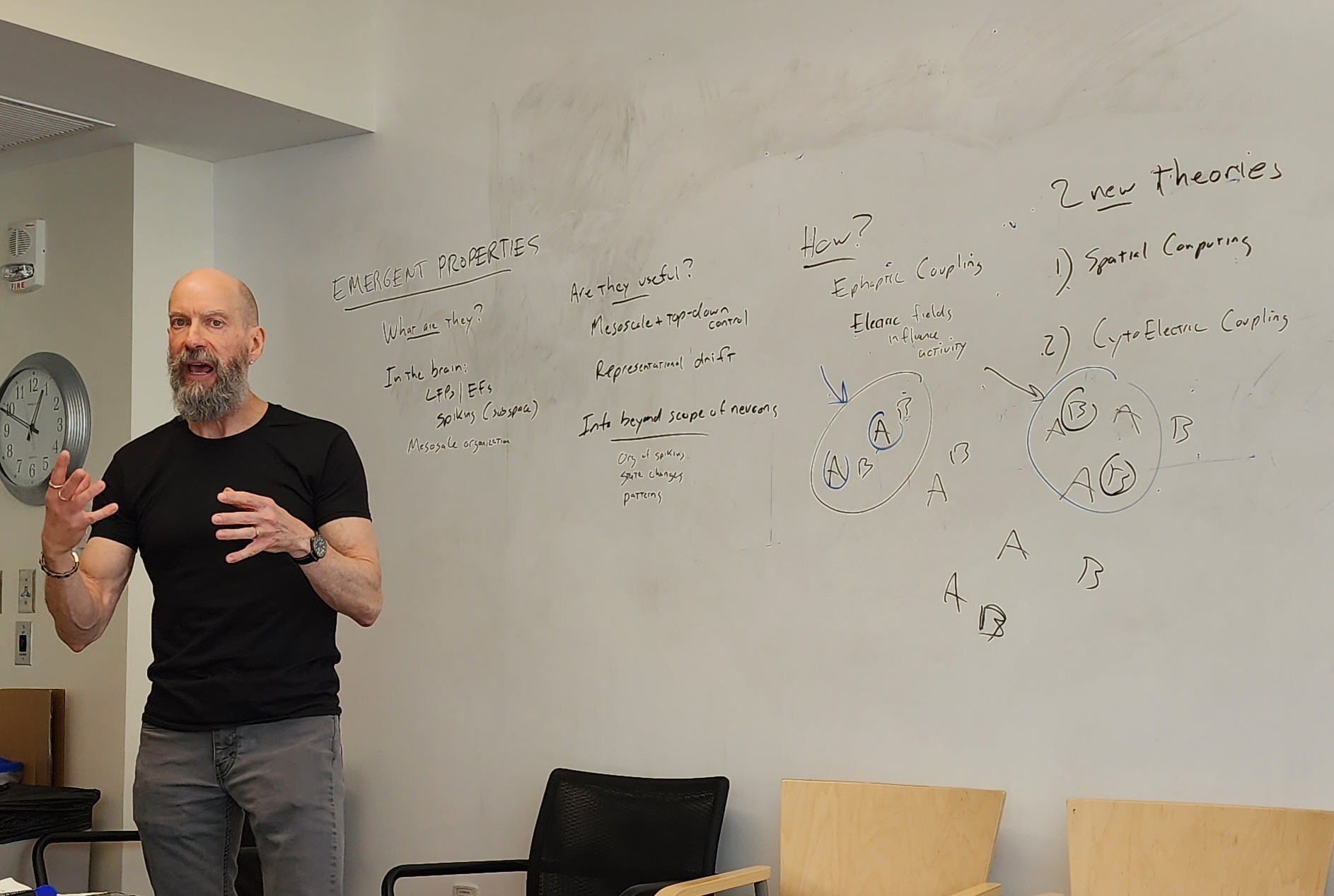 Earl K. Miller gestures as he talks while standing before a whiteboard where he has written several concepts including "cytoelectric coupling"