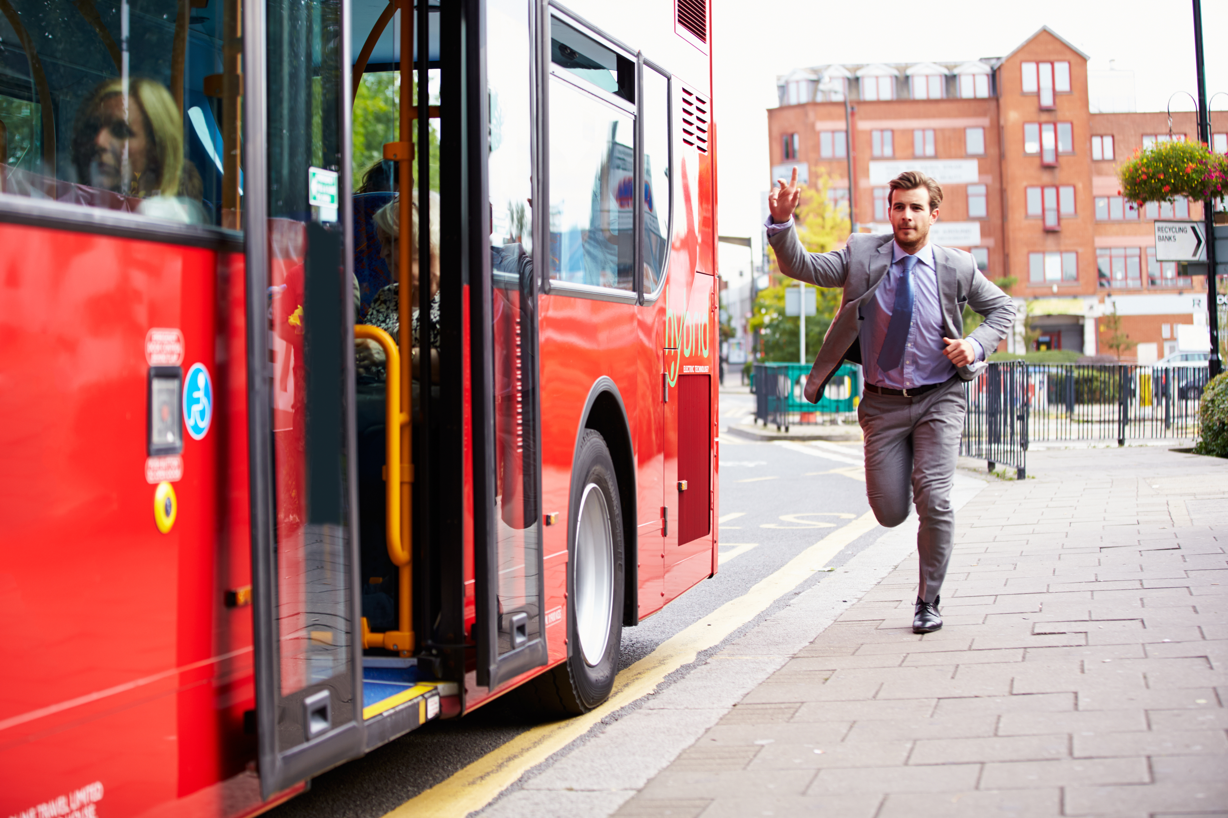 A man in a suit on a city street runs to catch up to a red bus at a stop.