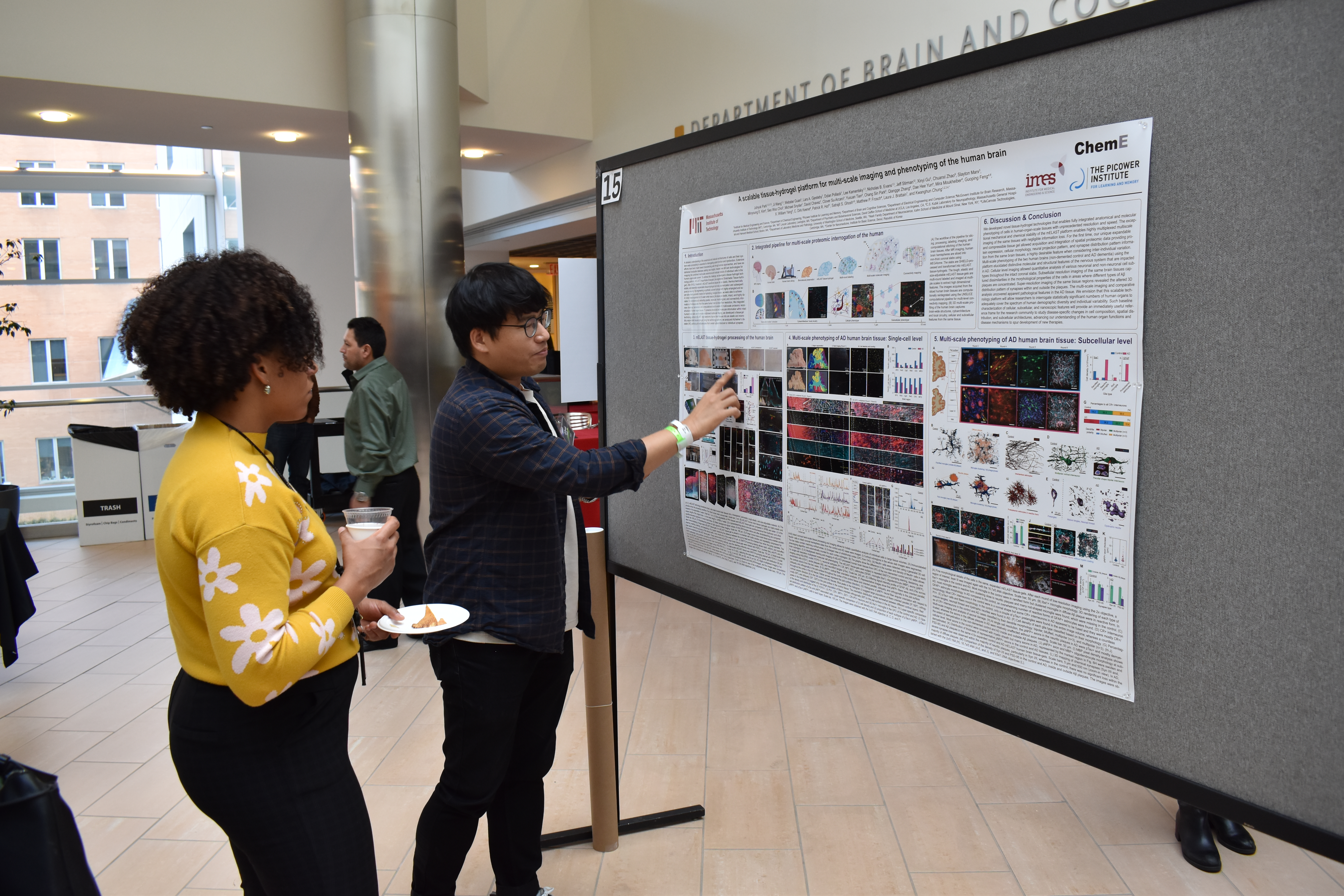 Juhyuk Park stands at a poster on a large gray easel board as an onlooker watches.