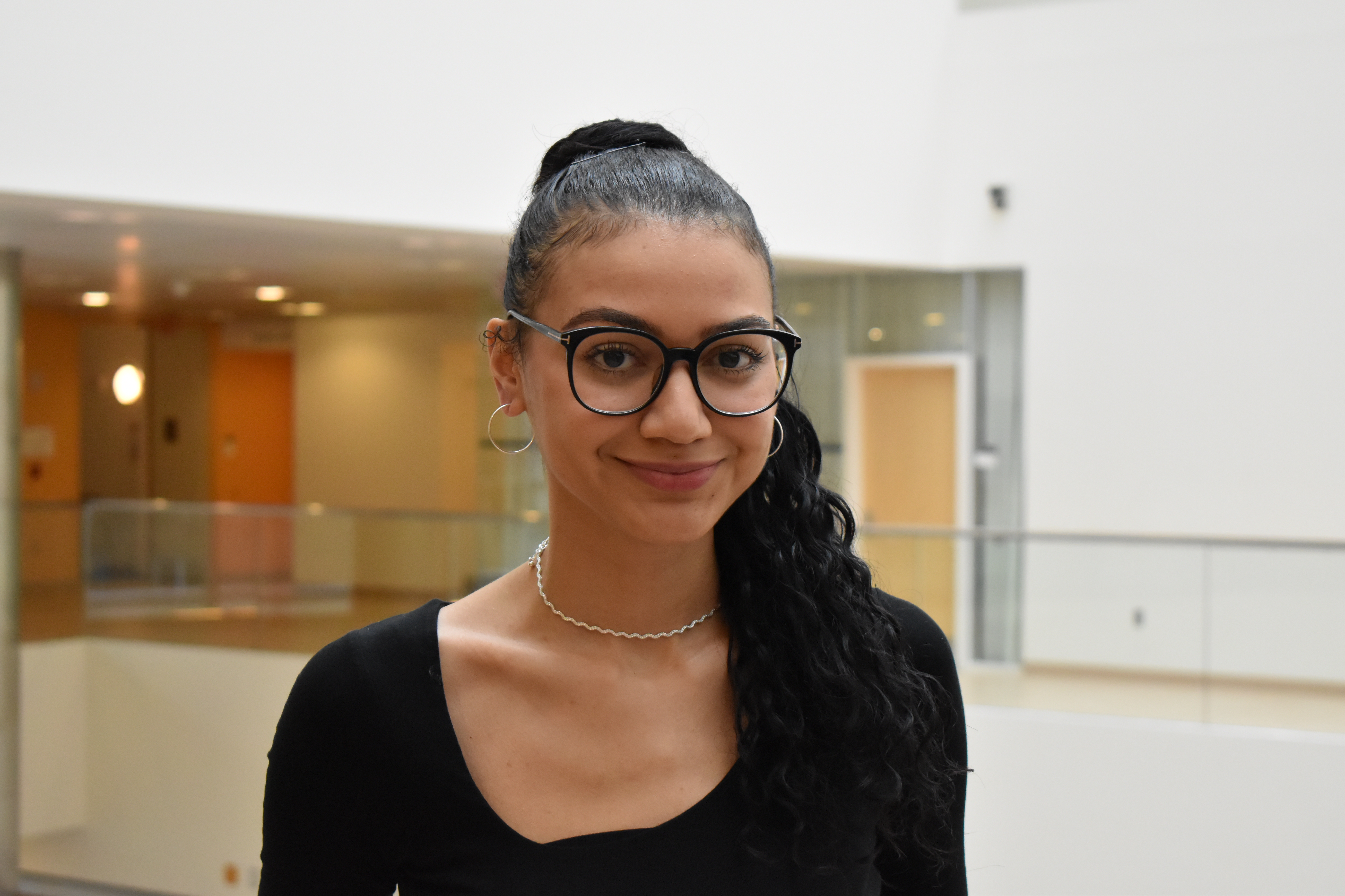 Mingus Zoller stands and smiles with a brightly lit open atrium behind her in MIT's Building 46.