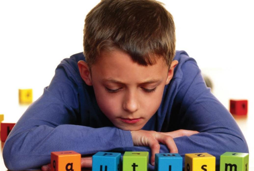 A boy sits with letter blocks that spell AUTISM