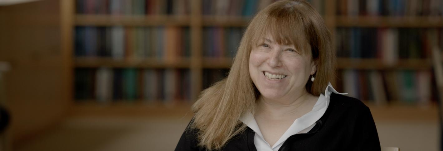 Elly Nedivi smiles as she sits in a chair in a library