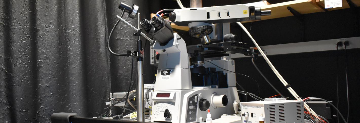 A white microscope with many wires and attachments sits on a black table