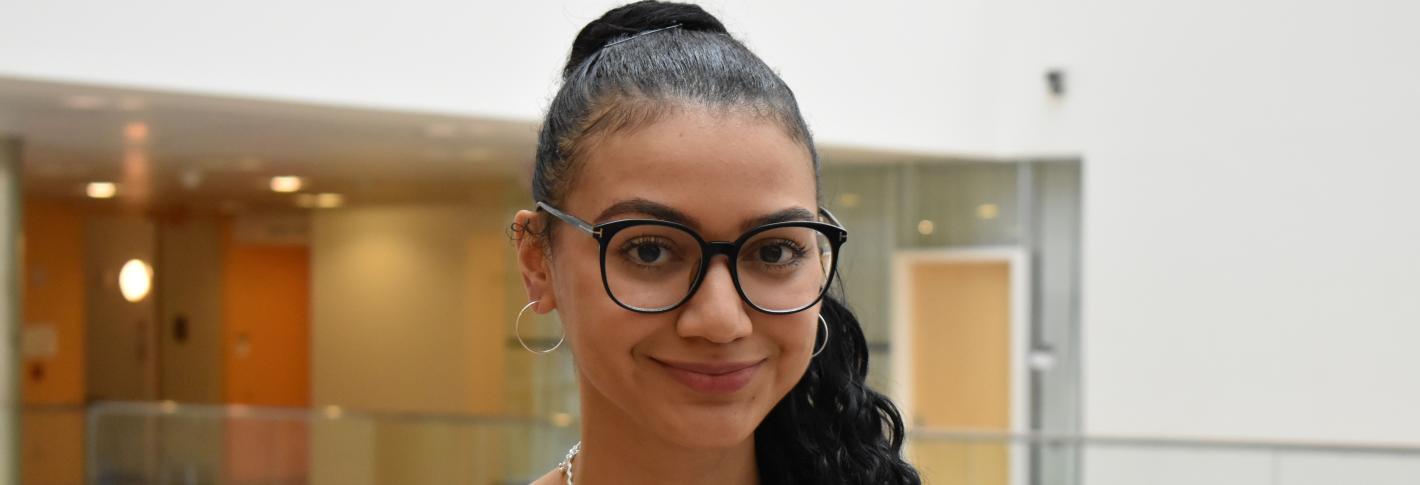 Mingus Zoller stands and smiles with a brightly lit open atrium behind her in MIT's Building 46.