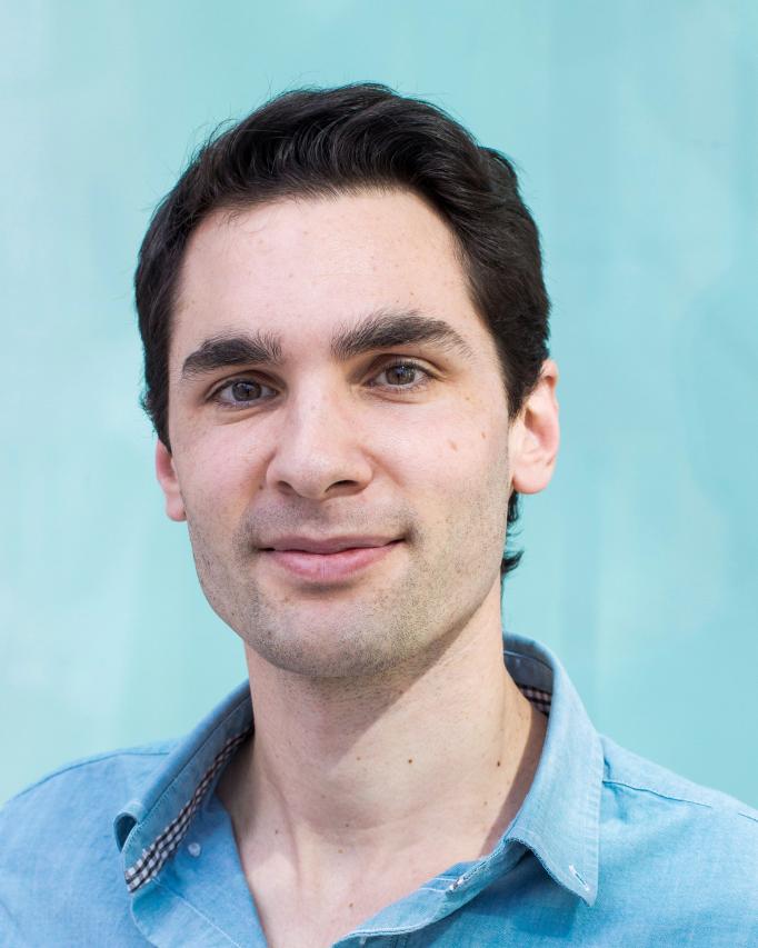 A portrait of Quentin Ferry with a blue background, wearing a blue dress shirt.